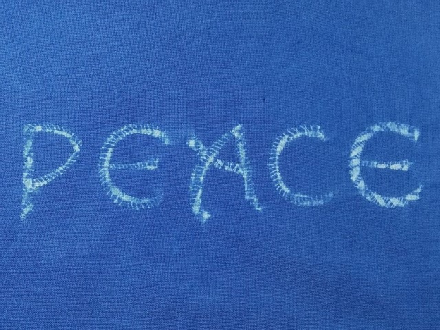 Dive in to Learn How to Create Words with Shibori Stitch 3 The word Peace stitched with shibori, white text against a blue ground